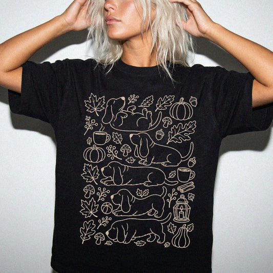 Model wearing a Black Comfort Colors® T-shirt with Basset Hound dogs with pumpkins, leaves, acorns, and woodland details