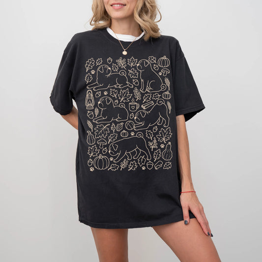 Model wearing a Black Comfort Colors® T-shirt with Pug dogs with pumpkins, leaves, acorns, and woodland details