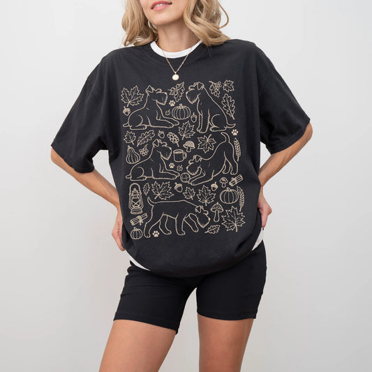 Model wearing a Black Comfort Colors® T-shirt with Schnauzer dogs with pumpkins, leaves, acorns, and woodland details