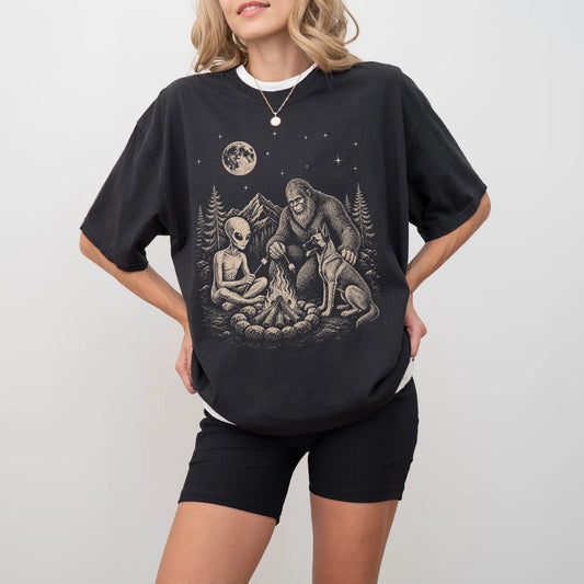 Model wearing a Black Comfort Colors® T-shirt showing Belgian Malinois camping with Bigfoot and an alien