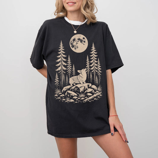 Model wearing a Black Comfort Colors® T-shirt with a Corgi howling beneath the moon and pine trees