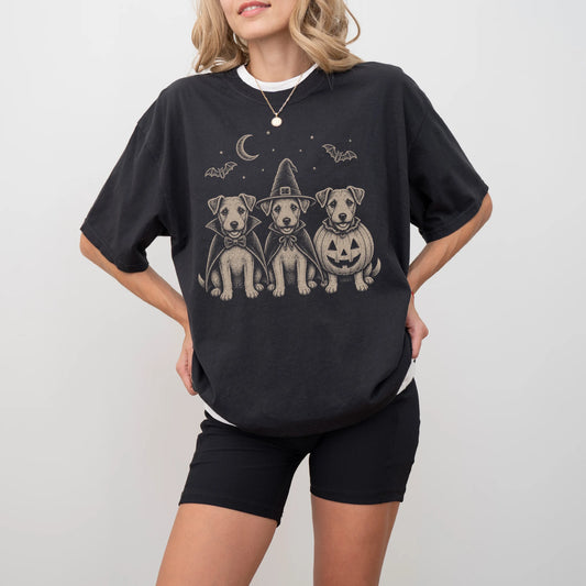Model wearing a Black Comfort Colors® T-shirt showing three Jack Russell dogs dressed for Halloween beneath bats and a cresce