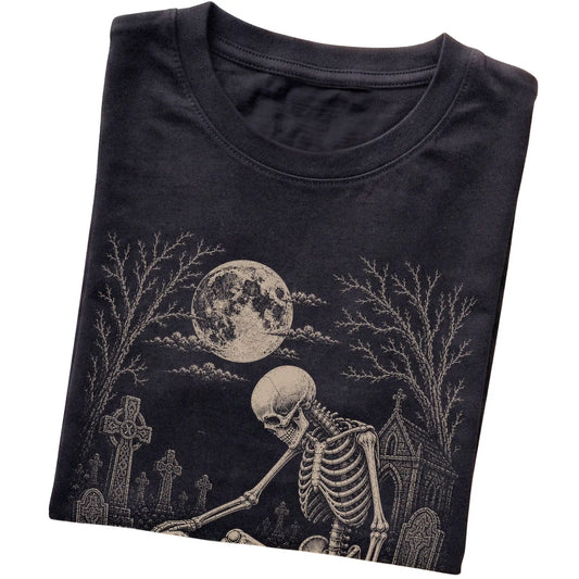 Folded Black T-shirt with a skeleton petting a Cavalier in a graveyard