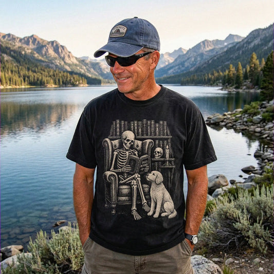 Model wearing a Black Comfort Colors® T-shirt showing skeleton reading in a library beside a Labradoodle
