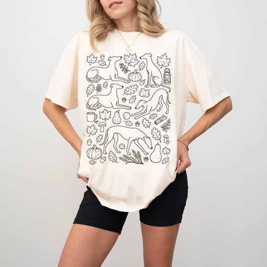 Model wearing a Ivory Comfort Colors® T-shirt with Greyhound dogs with pumpkins, leaves, acorns, and woodland details
