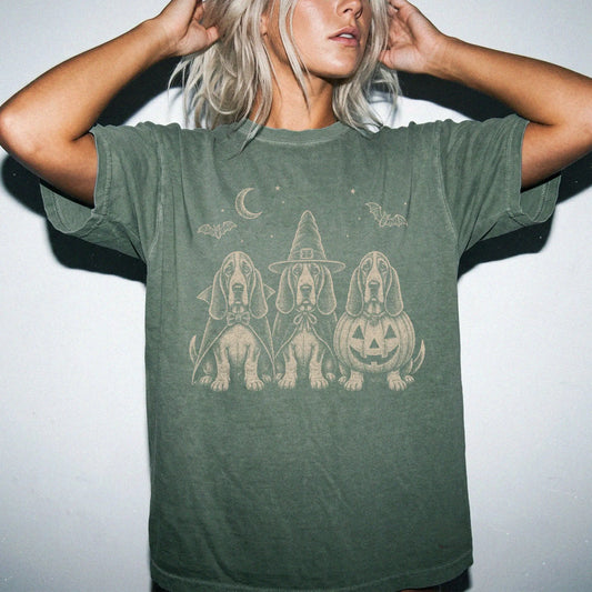 Model wearing a Moss Comfort Colors® T-shirt showing three Basset Hound dogs dressed for Halloween beneath bats and a crescen