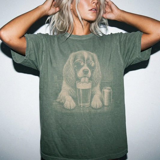 Model wearing a Moss Comfort Colors® t-shirt with Cavalier King Charles Spaniel sneaking a drink from a pint