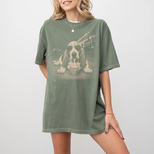 Model wearing a Moss Comfort Colors® T-shirt featuring Basset Hound with iced coffee in a retro grunge design