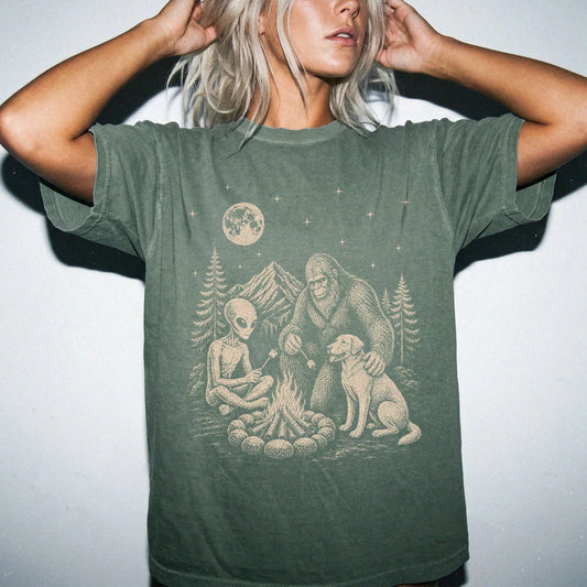 Model wearing a Moss Comfort Colors® T-shirt showing Labrador Retriever camping with Bigfoot and an alien