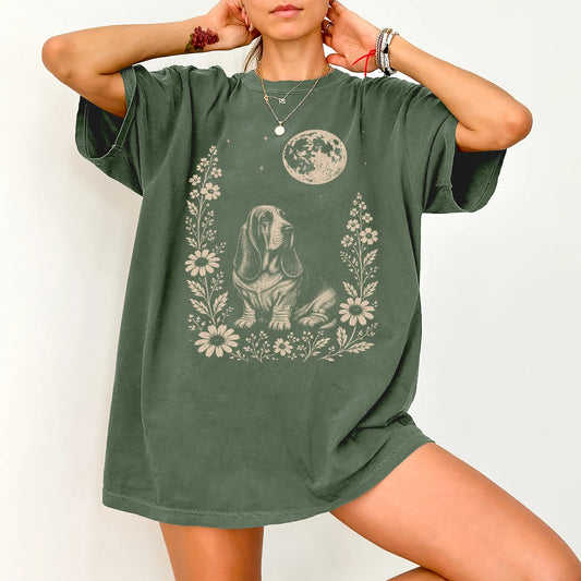 Model wearing a Moss Comfort Colors® T-shirt featuring Basset Hound framed by flowers beneath the moon