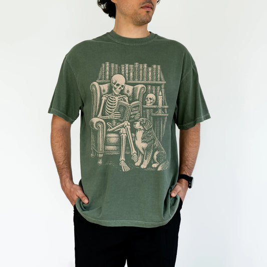 Model wearing a Moss Comfort Colors® T-shirt showing skeleton reading in a library beside a Bernese Mountain Dog