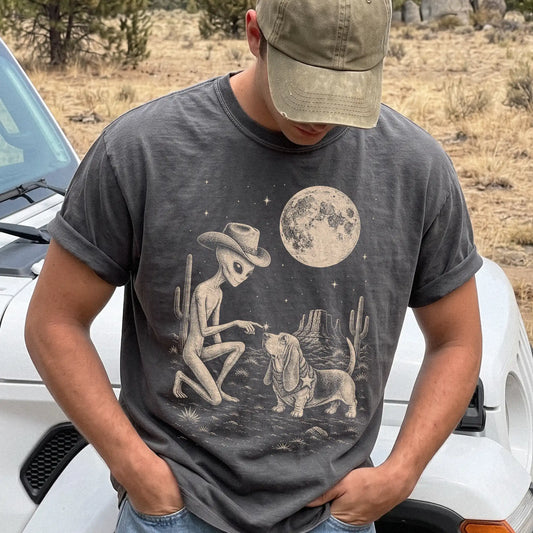 Model wearing a Pepper Comfort Colors® T-shirt with cowboy alien fist-bumping a basset hound beneath the moon