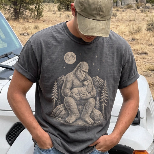 Model wearing a Pepper Comfort Colors® T-shirt showing Bigfoot holding a Cocker Spaniel