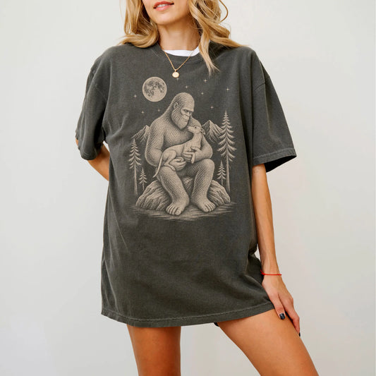 Model wearing a Pepper Comfort Colors® T-shirt showing Bigfoot holding a Whippet