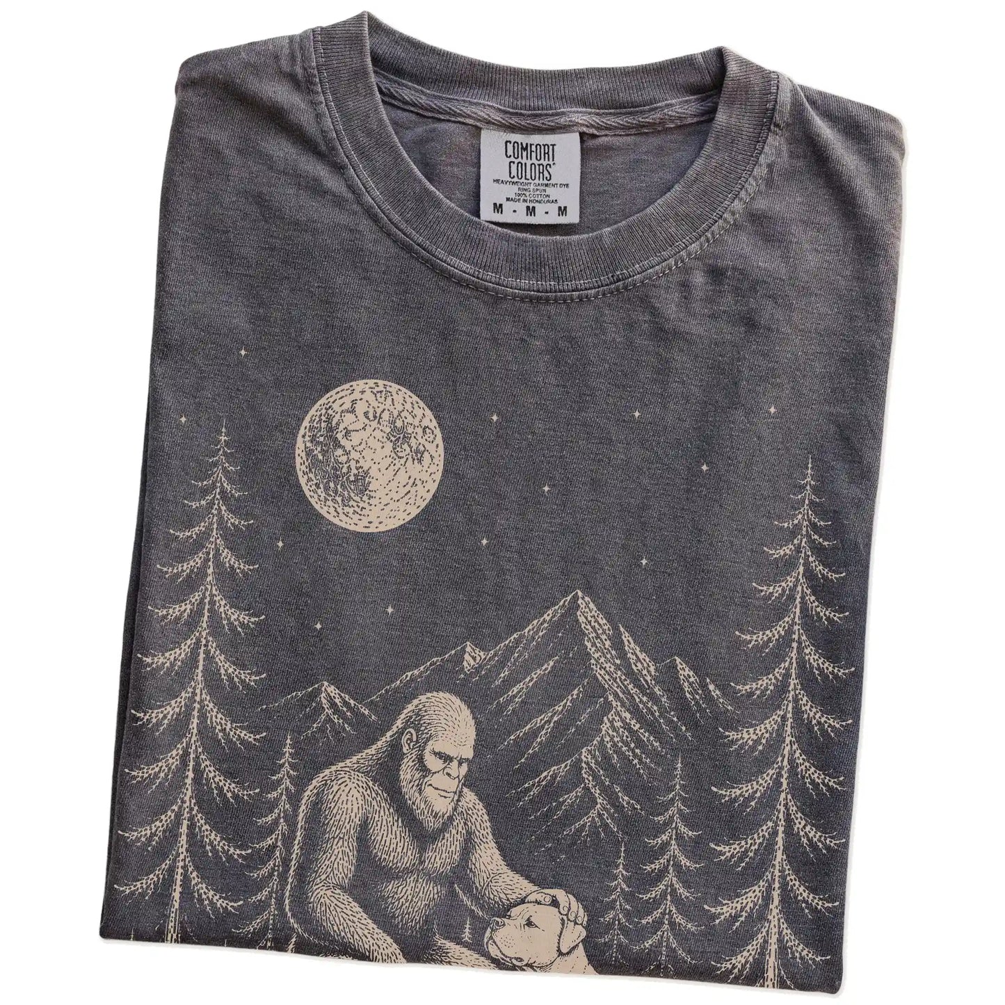 Folded Pepper Comfort Colors® T-shirt showing bigfoot petting a american bulldog beneath the moon in a pine forest