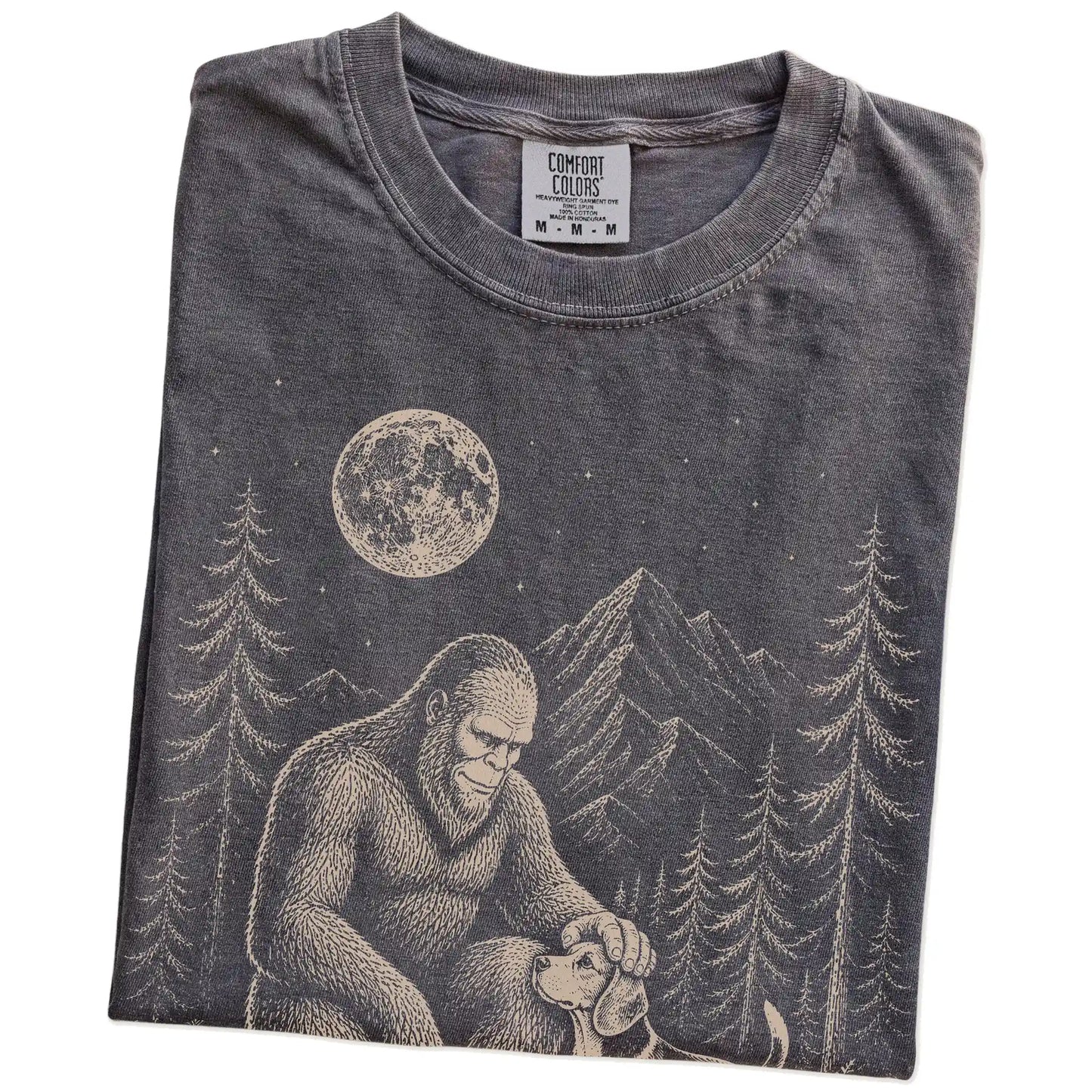 Folded Pepper Comfort Colors® T-shirt showing bigfoot petting a beagle beneath the moon in a pine forest