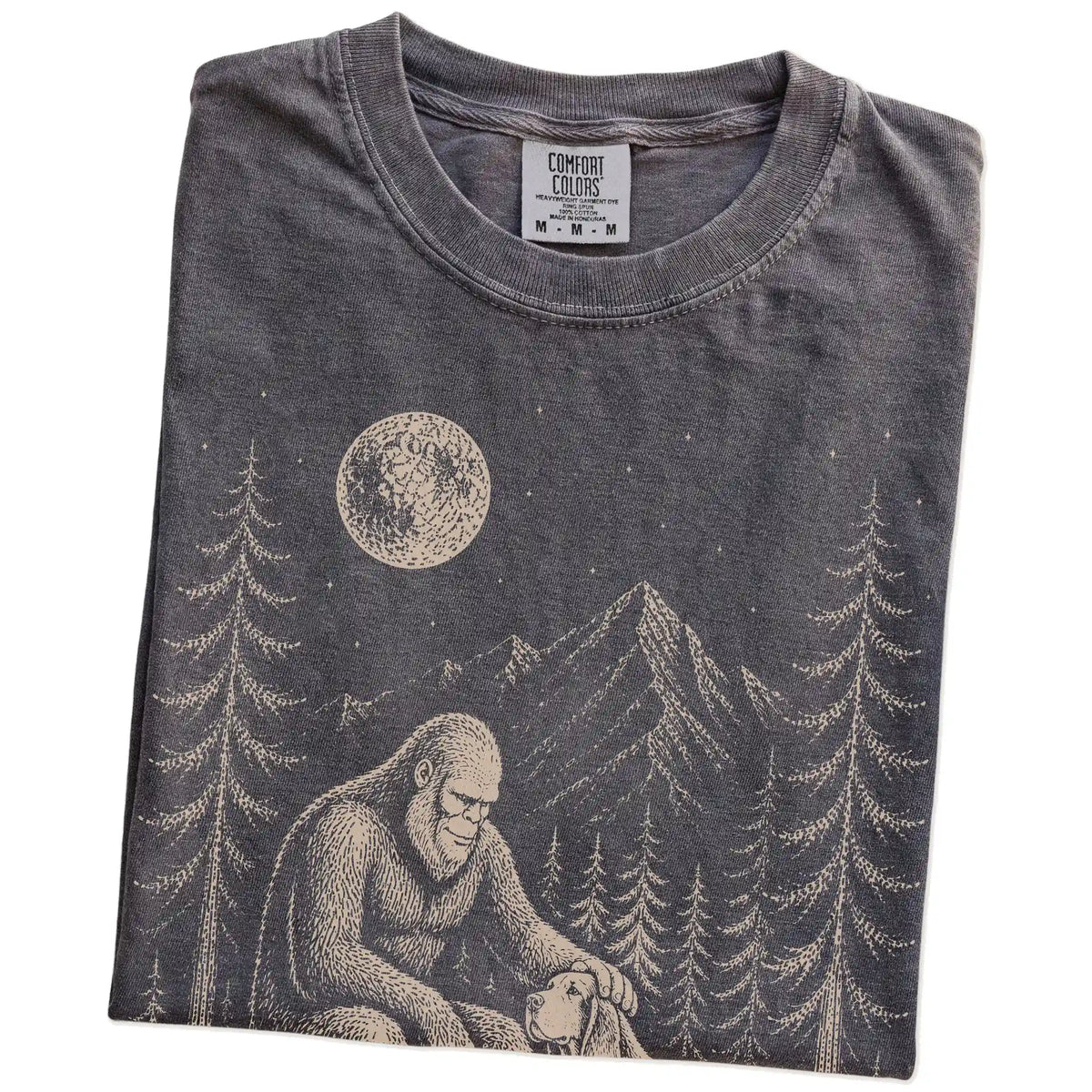 Folded Pepper Comfort Colors® T-shirt showing bigfoot petting a bloodhound beneath the moon in a pine forest