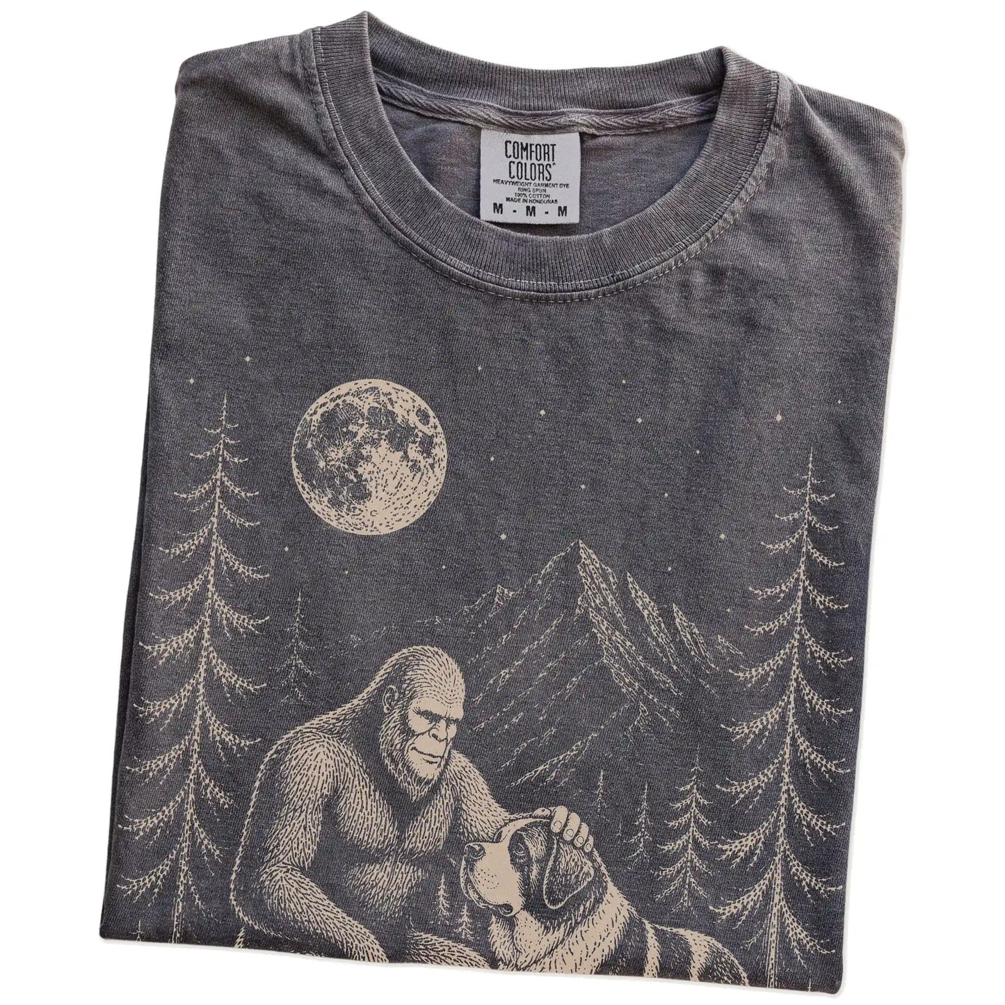 Folded Pepper Comfort Colors® T-shirt showing bigfoot petting a saint bernard beneath the moon in a pine forest