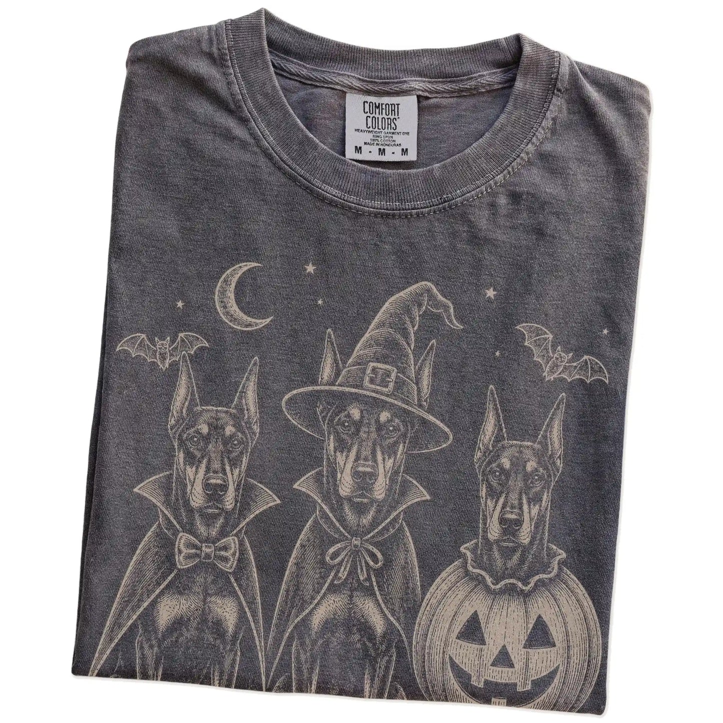 Folded Pepper Comfort Colors® T-shirt showing three Doberman dogs dressed for Halloween beneath bats and a crescent moon