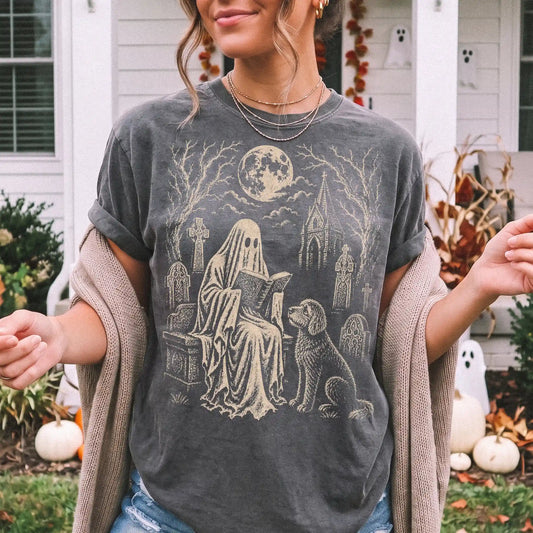 Model wearing a Pepper Comfort Colors® T-shirt showing Goldendoodle beside a reading ghost in a moonlit graveyard