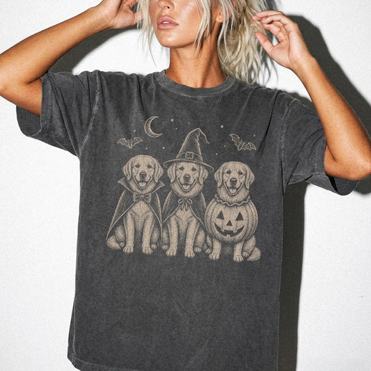 Model wearing a Pepper Comfort Colors® T-shirt showing three Golden Retriever dogs dressed for Halloween beneath bats and a c