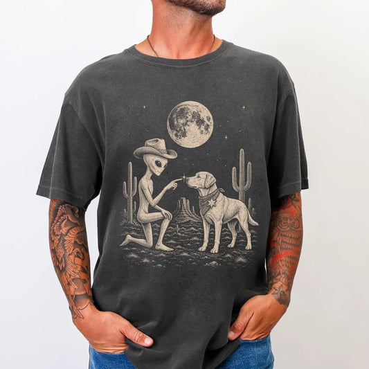 Model wearing a Pepper Comfort Colors® T-shirt with cowboy alien fist-bumping a labrador retriever beneath the moon