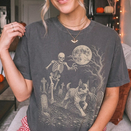 Model wearing a Pepper Comfort Colors® T-shirt showing Blue Heeler running through a moonlit graveyard with a chasing skeleto