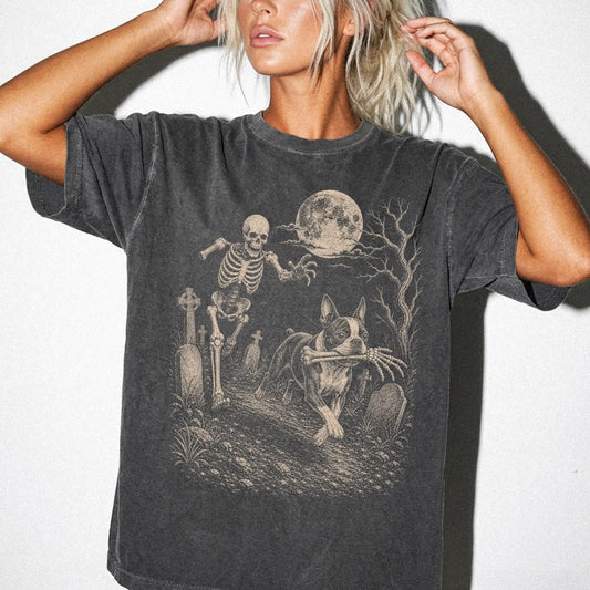 Model wearing a Pepper Comfort Colors® T-shirt showing Boston Terrier running through a moonlit graveyard with a chasing skel
