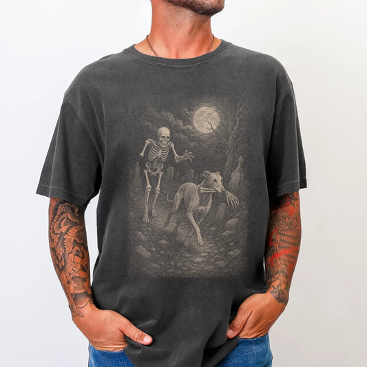 Model wearing a Pepper Comfort Colors® T-shirt showing Greyhound running through a moonlit graveyard with a chasing skeleton