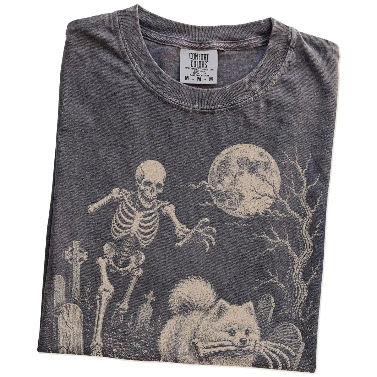 Folded Pepper Comfort Colors® T-shirt showing Pomeranian running through a moonlit graveyard with a chasing skeleton