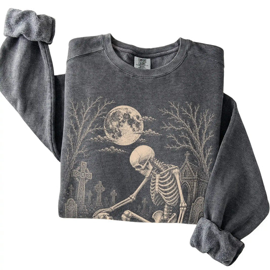 Folded Pepper sweatshirt with a skeleton petting a Cavalier in a graveyard