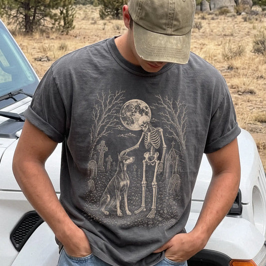 Model wearing a Pepper Comfort Colors® T-shirt showing Doberman sharing a quiet cemetery moment with a friendly skeleton