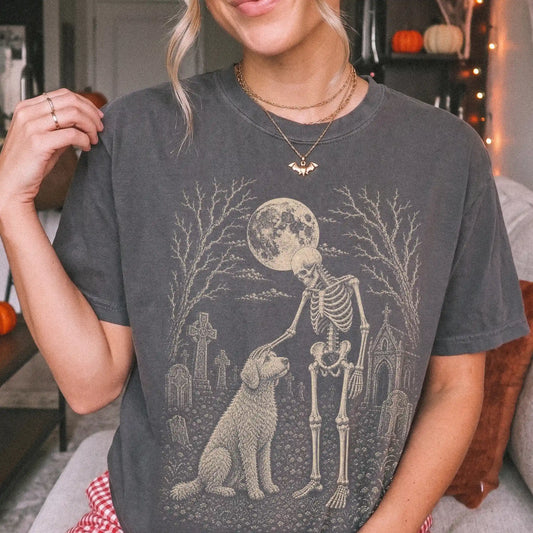 Model wearing a Pepper Comfort Colors® T-shirt showing Goldendoodle sharing a quiet cemetery moment with a friendly skeleton
