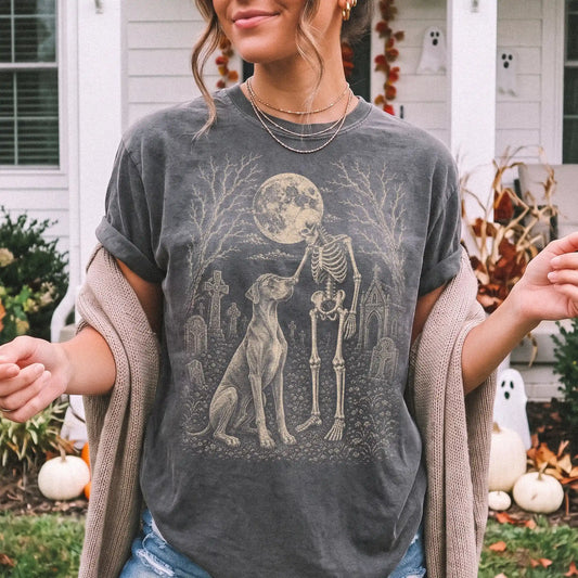 Model wearing a Pepper Comfort Colors® T-shirt showing Great Dane sharing a quiet cemetery moment with a friendly skeleton