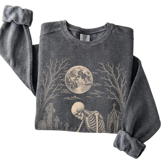 Folded Pepper sweatshirt with a skeleton petting a Maltese in a graveyard