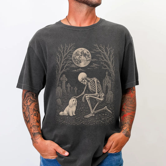 Model wearing a Pepper Comfort Colors® T-shirt showing Maltese sharing a quiet cemetery moment with a friendly skeleton