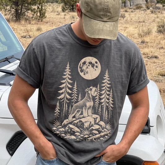 Model wearing a Pepper Comfort Colors® T-shirt with a Standard Schnauzer howling beneath the moon and pine trees