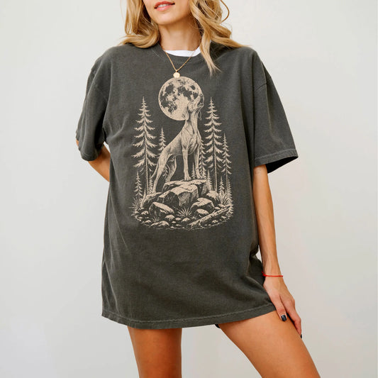 Model wearing a Pepper Comfort Colors® T-shirt with a Weimaraner howling beneath the moon and pine trees