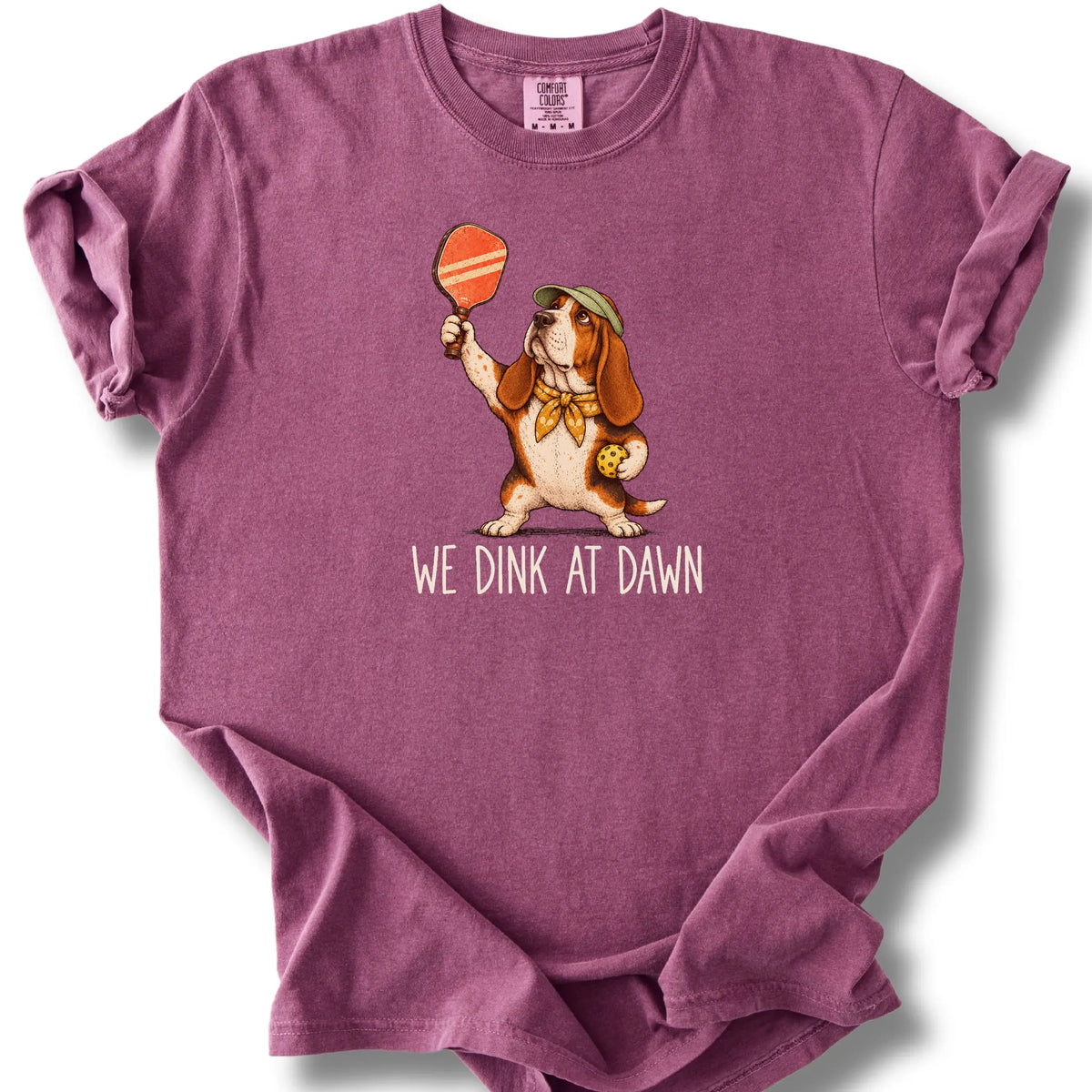 Basset Hound with a pickleball paddle and ball on a Berry Comfort Colors® T-shirt with We Dink at Dawn text