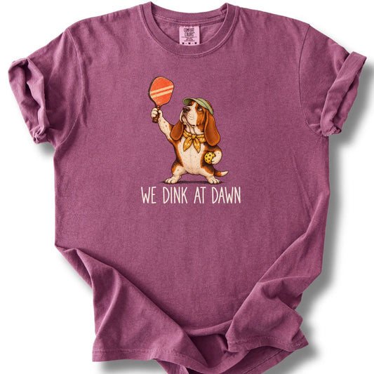 Basset Hound with a pickleball paddle and ball on a Berry Comfort Colors® T-shirt with We Dink at Dawn text