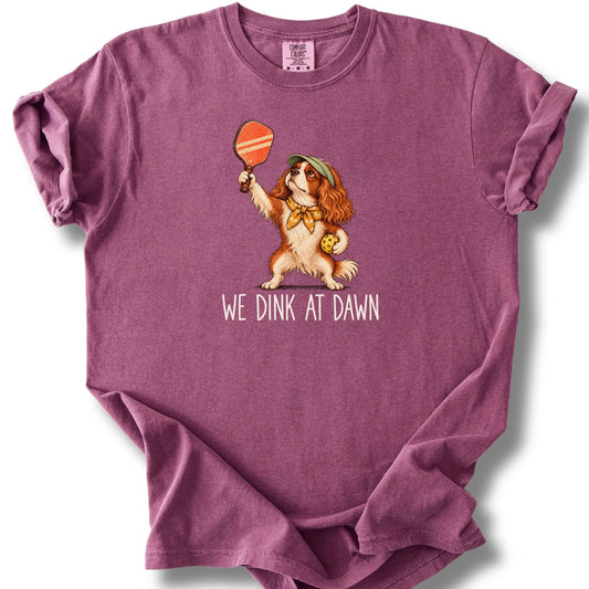 Cavalier with a pickleball paddle and ball on a Berry Comfort Colors® T-shirt with We Dink at Dawn text