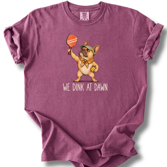 French Bulldog with a pickleball paddle and ball on a Berry Comfort Colors® T-shirt with We Dink at Dawn text