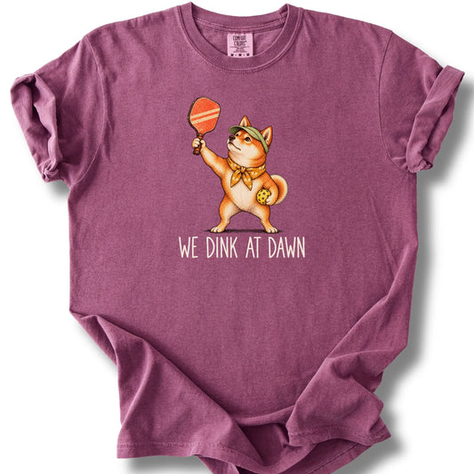 Shiba Inu with a pickleball paddle and ball on a Berry Comfort Colors® T-shirt with We Dink at Dawn text