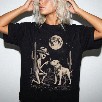 Model wearing a Black Comfort Colors® T-shirt with cowboy alien fist-bumping a american bulldog beneath the moon