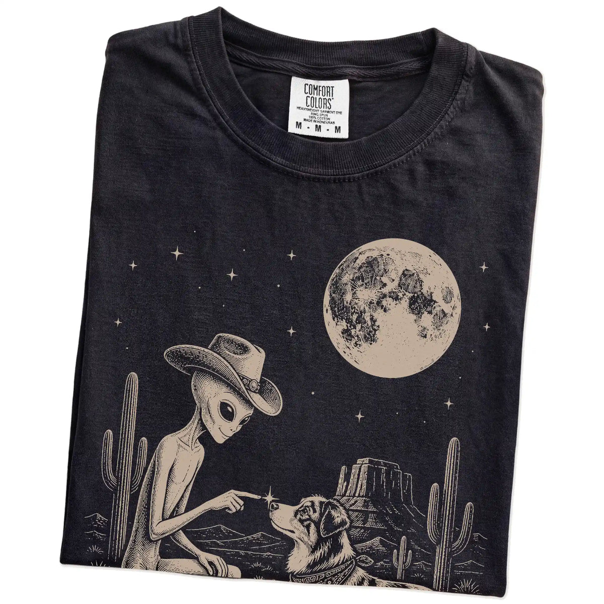 Folded Black Comfort Colors® T-shirt showing cowboy alien fist-bumping a australian shepherd beneath the moon
