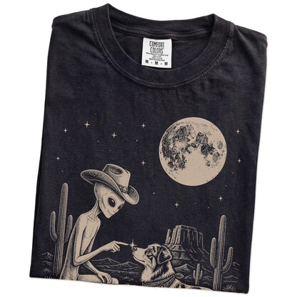 Folded Black Comfort Colors® T-shirt showing cowboy alien fist-bumping a australian shepherd beneath the moon
