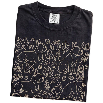 Folded Black Comfort Colors® T-shirt showing Boston Terrier dogs with pumpkins, leaves, acorns, and woodland details