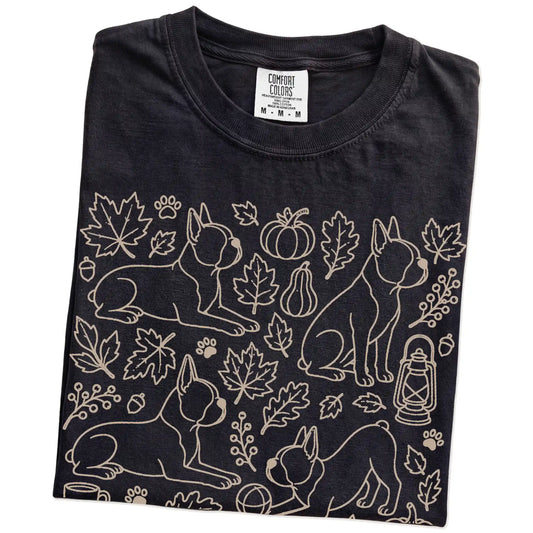 Folded Black Comfort Colors® T-shirt showing Boston Terrier dogs with pumpkins, leaves, acorns, and woodland details