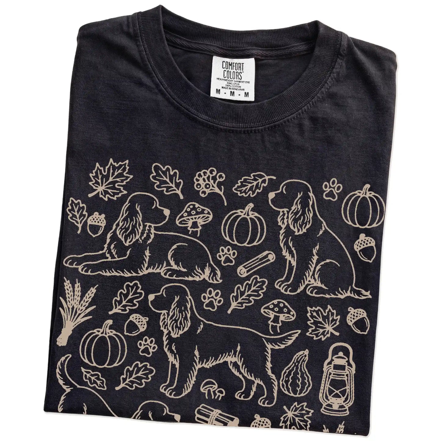 Folded Black Comfort Colors® T-shirt showing Cocker Spaniel dogs with pumpkins, leaves, acorns, and woodland details