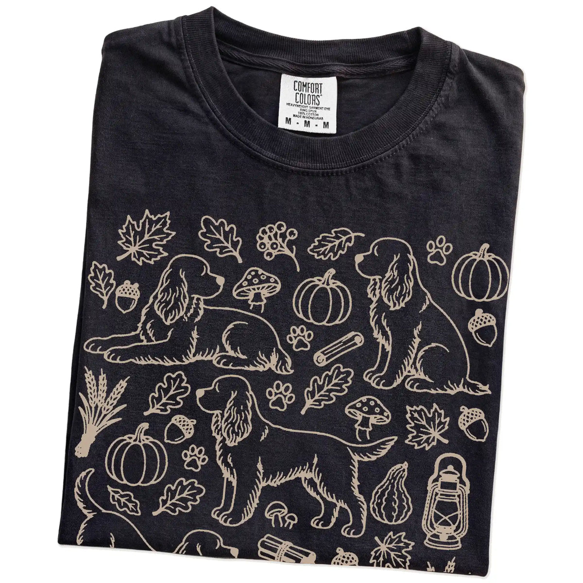 Folded Black Comfort Colors® T-shirt showing Cocker Spaniel dogs with pumpkins, leaves, acorns, and woodland details